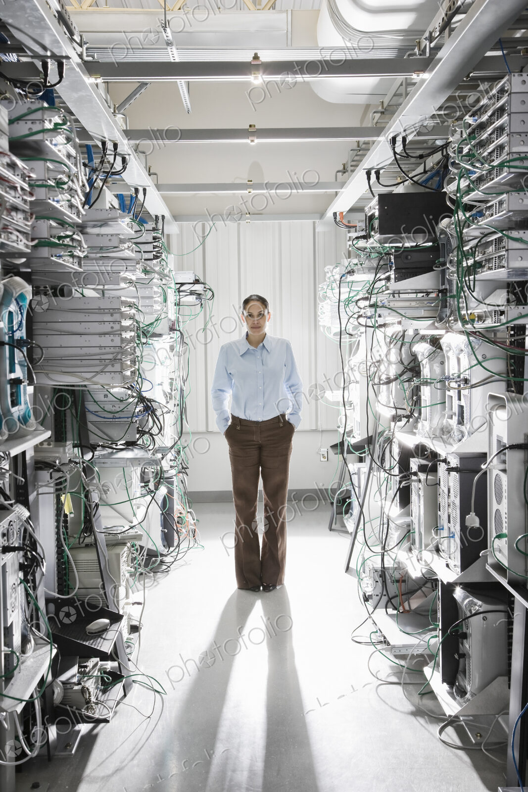 Caucasian woman technician working in the aisle of a computer server farm.