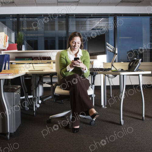 Caucasian woman texting on her cell phone in her cubicle office space.