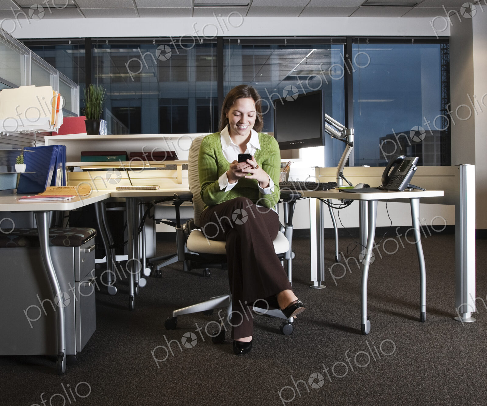 Caucasian woman texting on her cell phone in her cubicle office space.