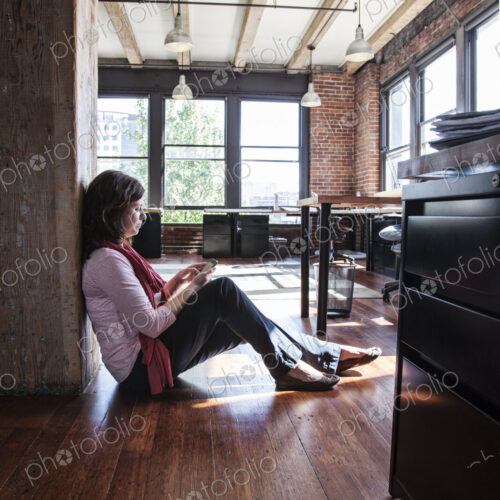 Caucasian woman using phone while sitting on the floor of a creative office.