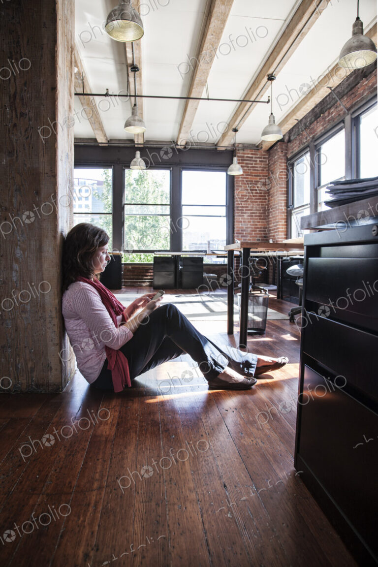 Caucasian woman using phone while sitting on the floor of a creative office.