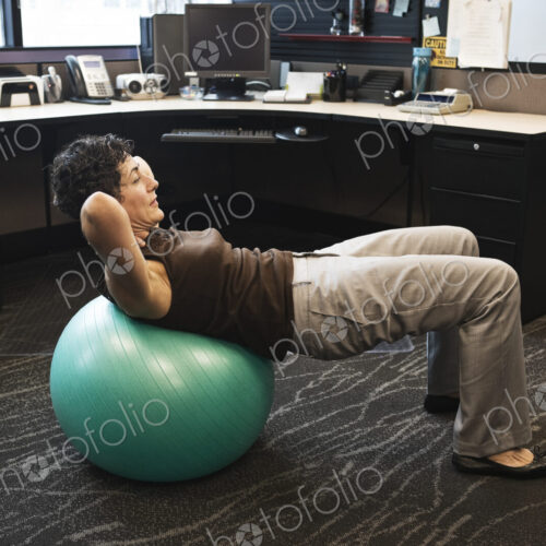 Caucasian woman working out on a Bosu Ball in her office cubicle. Caucasian woman working out on a Bosu Ball in her office cubicle.