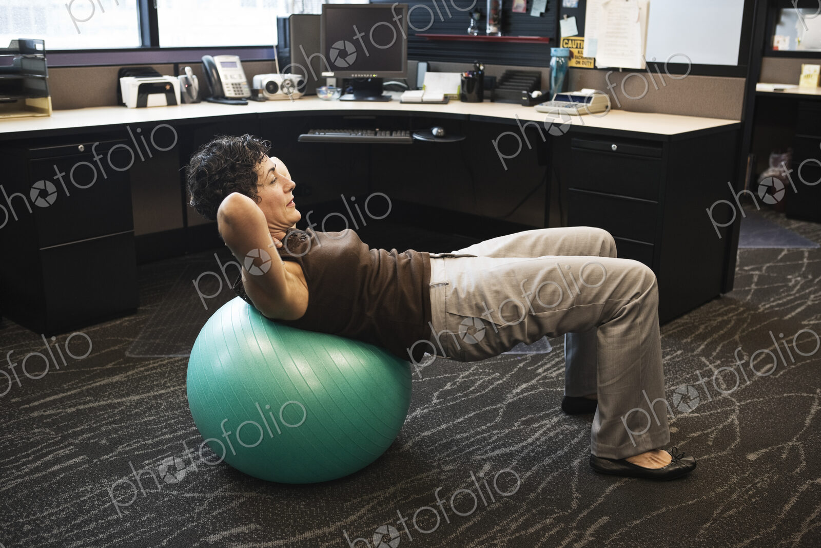 Caucasian woman working out on a Bosu Ball in her office cubicle.