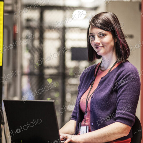 Caucasiasn woman technician working in a large computer server farm.
