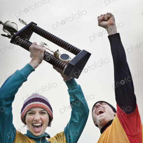 Caucasin woman and man celebrating a team win in a sporting event with a trophy in hand.