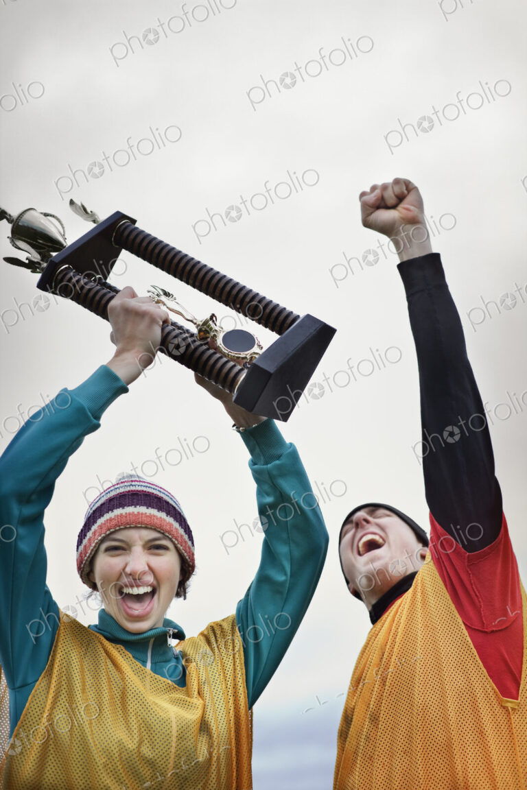 Caucasin woman and man celebrating a team win in a sporting event with a trophy in hand.