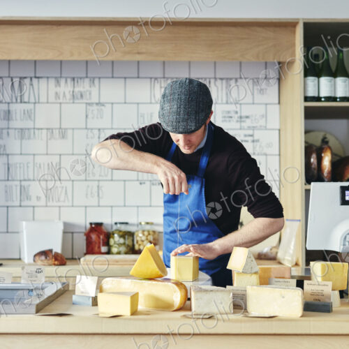 Cheesemonger cutting cheese with cheese wire surrounded by a variety of cheese on…