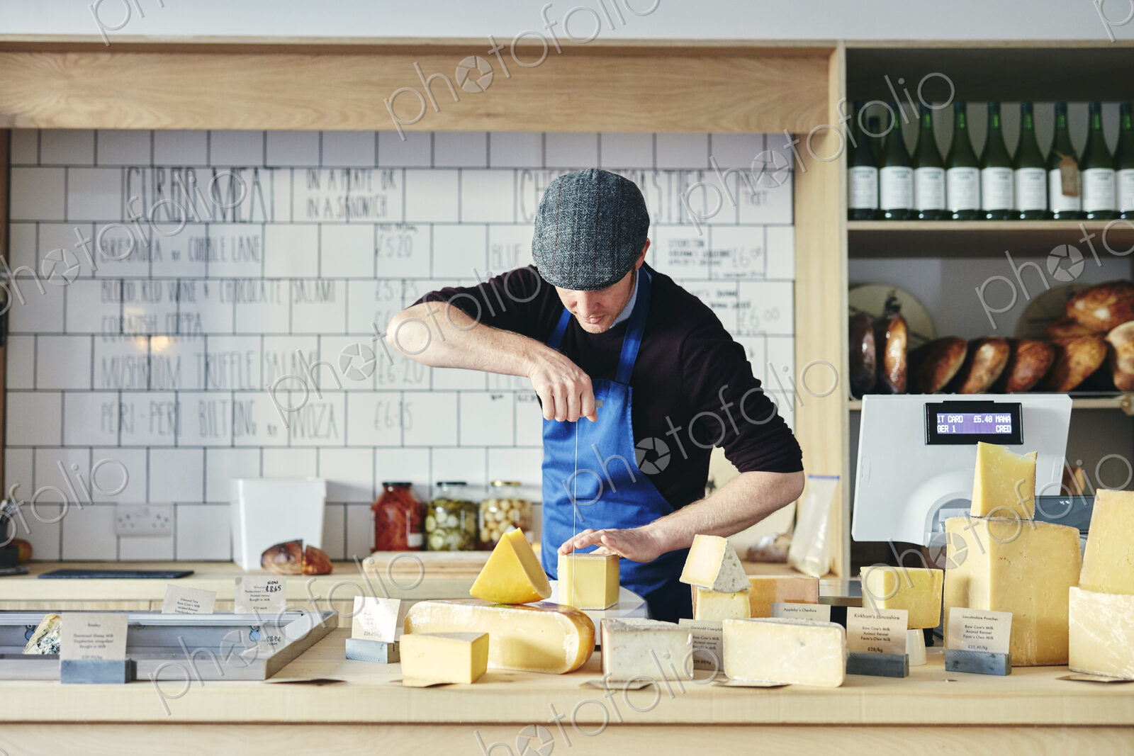 Cheesemonger cutting cheese with cheese wire surrounded by a variety of cheese on…