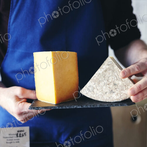 Cheesemonger holding slate displaying two different cheeses