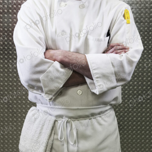 Chef in a white jacket and apron around his waist with arms folded. Mid section. Chef in a white jacket and apron around his waist with arms folded. Mid section.
