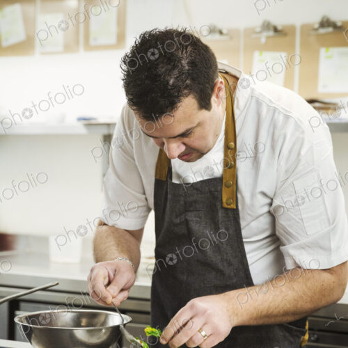 Chef standing in the kitchen in a small hotel, plating up a dish of vegetables.