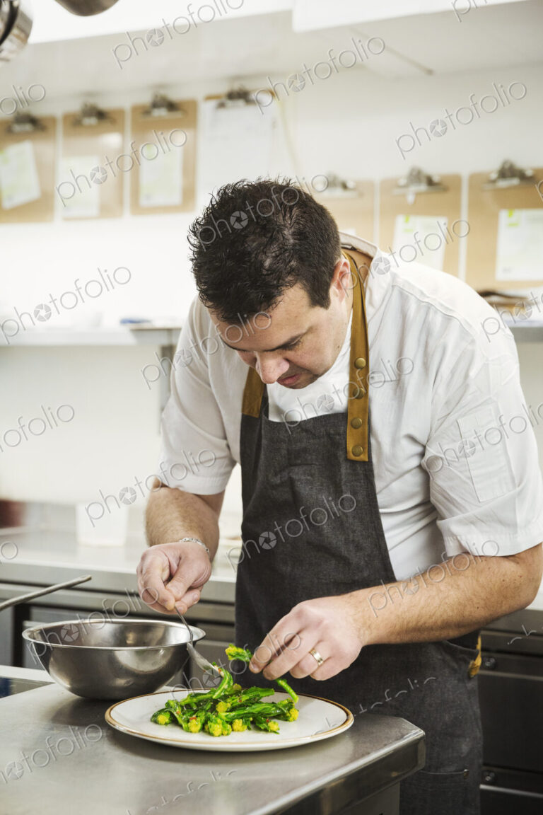Chef standing in the kitchen in a small hotel, plating up a dish of vegetables.