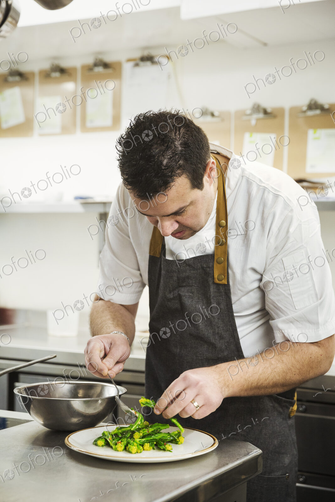 Chef standing in the kitchen in a small hotel, plating up a dish of vegetables.