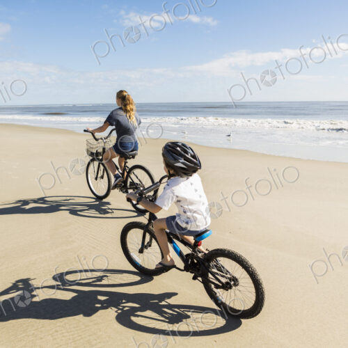 Children cycling on the sand by the water, a boy and girl.