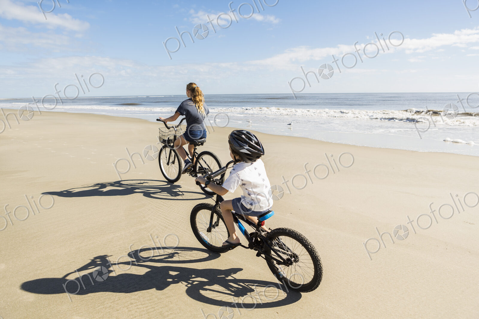 Children cycling on the sand by the water, a boy and girl.