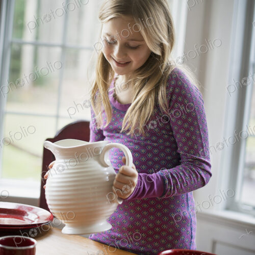Children in a family home. A girl holding a white pottery jug. Table laid with crockery. Children in a family home. A girl holding a white pottery jug. Table laid with crockery.