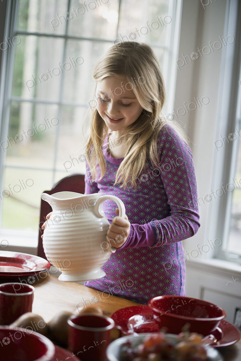 Children in a family home. A girl holding a white pottery jug. Table laid with crockery.