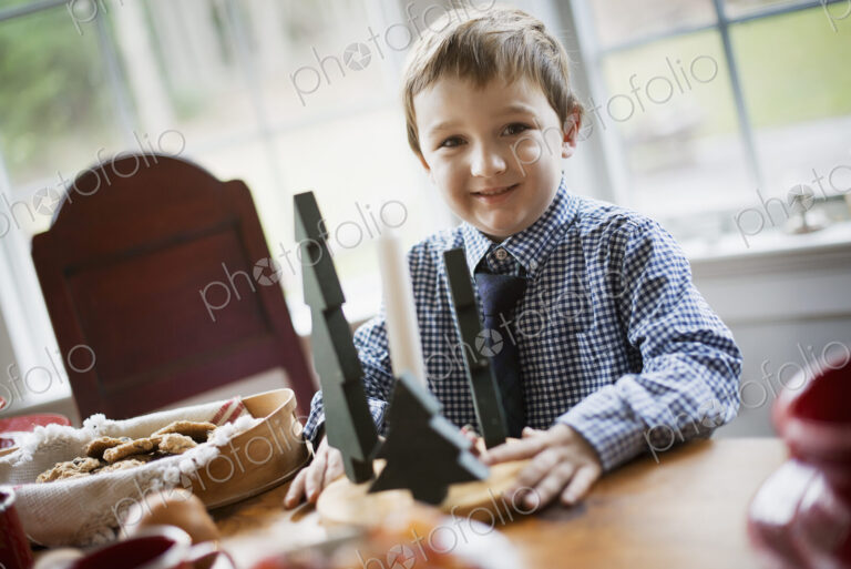 Children in a family home. A young boy at a table, beside a large tray of biscuits.…