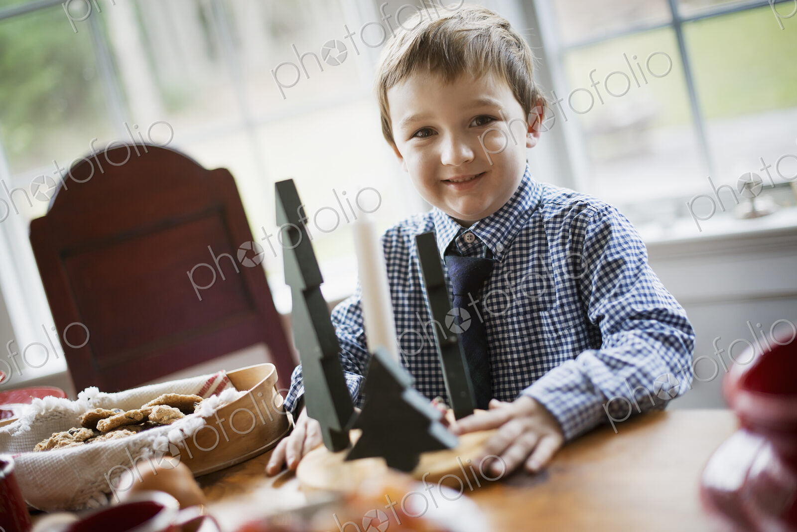 Children in a family home. A young boy at a table, beside a large tray of biscuits.…