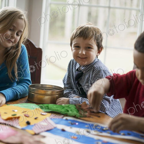 Children in a family home. Three children creating pictures, with glue and stickers.…