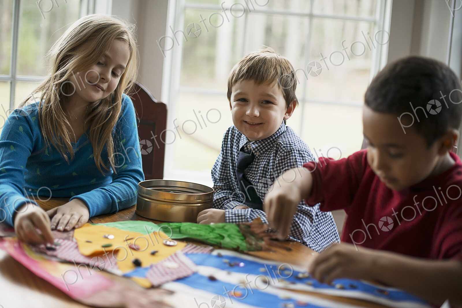 Children in a family home. Three children creating pictures, with glue and stickers.…