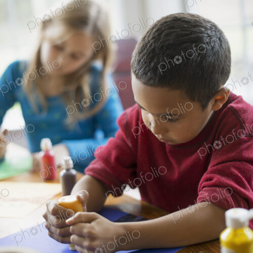 Children in a family home. Two children sitting at the table, using paint and paper to… Children in a family home. Two children sitting at the table, using paint and paper to…