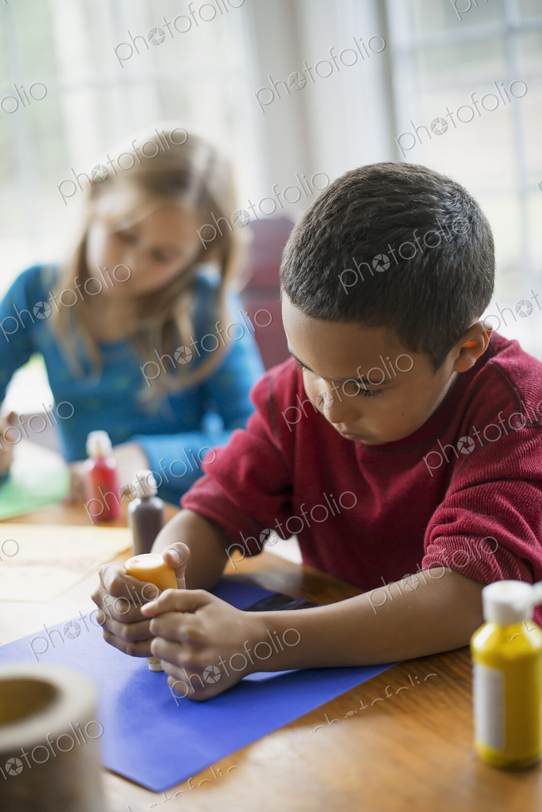 Children in a family home. Two children sitting at the table, using paint and paper to…