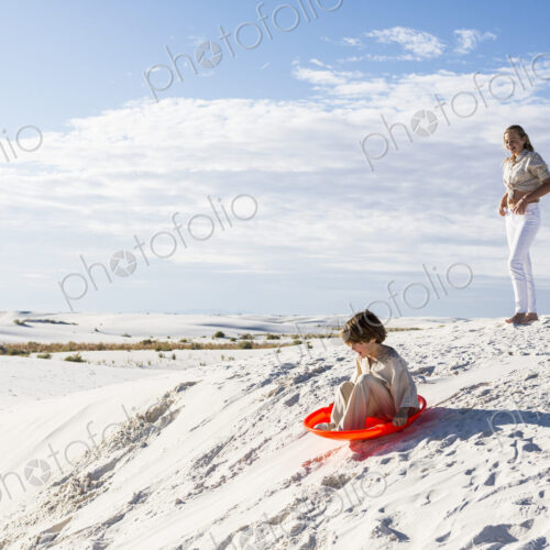 Children playing in sand dunes landscape, one on an orange sled. Children playing in sand dunes landscape, one on an orange sled.