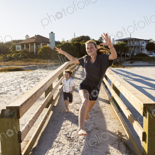 Children running across wooden bridge over sand Children running across wooden bridge over sand
