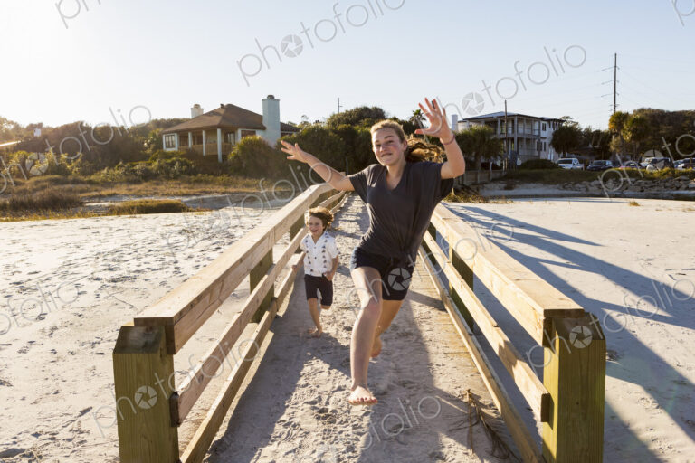 Children running across wooden bridge over sand