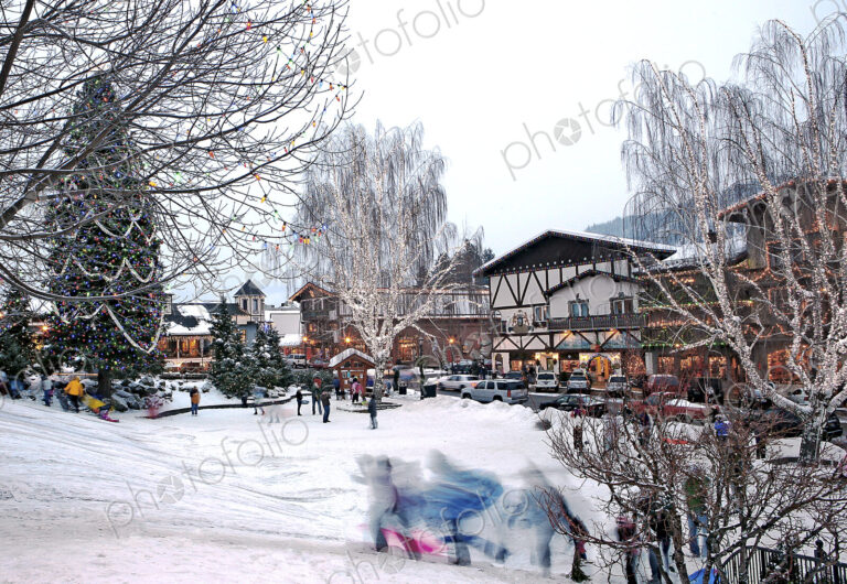 Children running on snowy slope in front of skiing resort buildings.