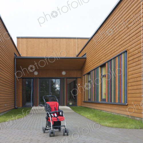 Child's buggy pushchair with a red seat outside a modern day care or pre-school building Child's buggy pushchair with a red seat outside a modern day care or pre-school building