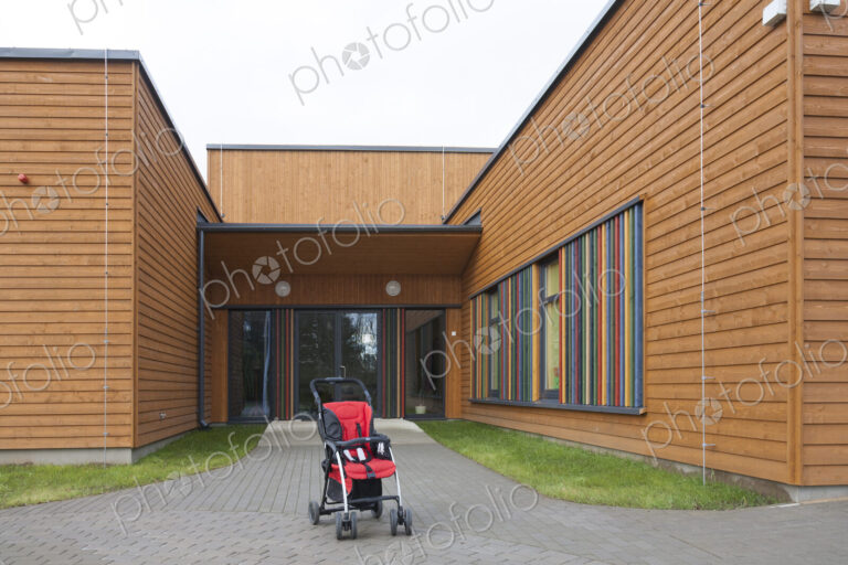 Child's buggy pushchair with a red seat outside a modern day care or pre-school building