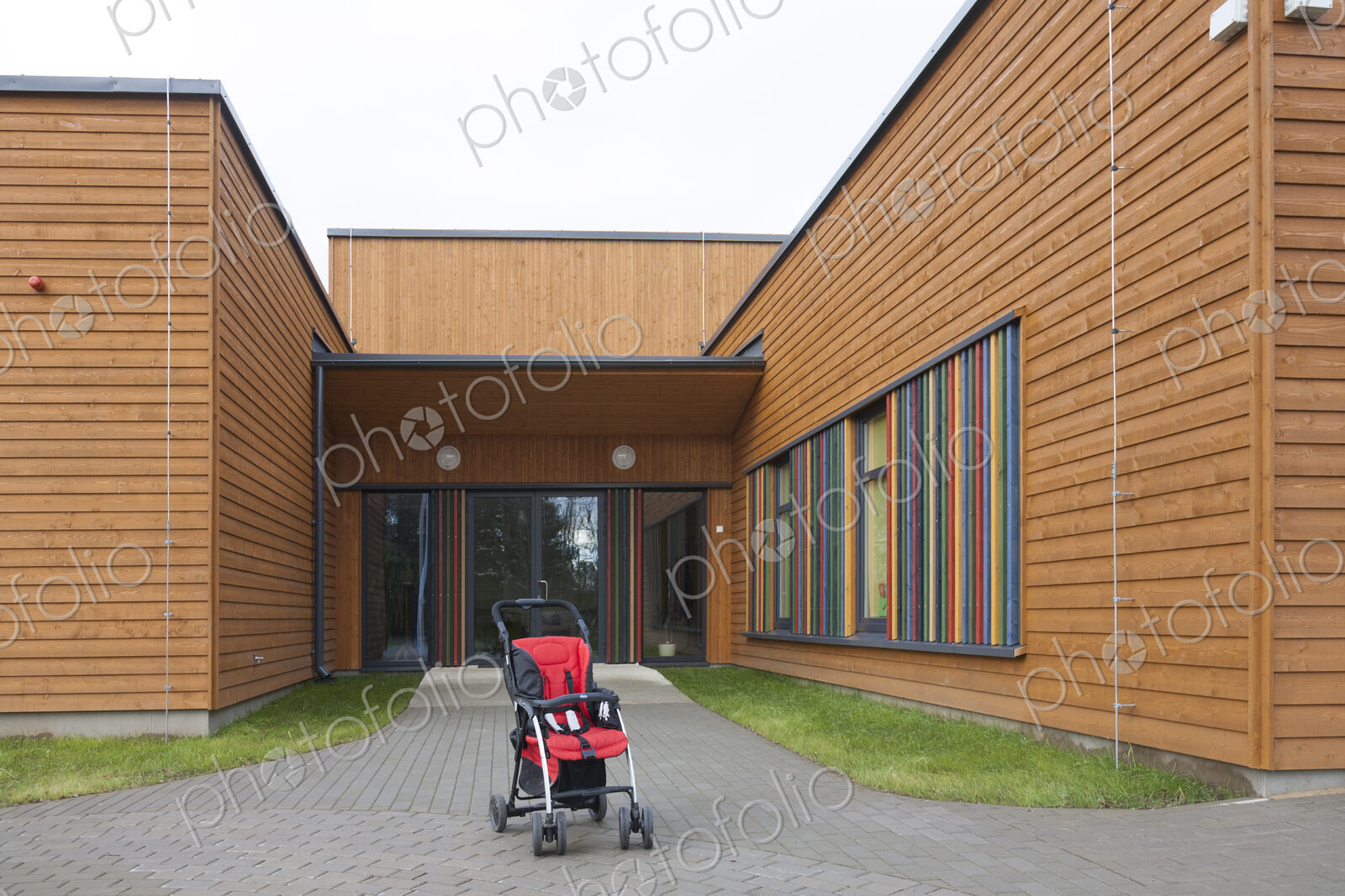Child’s buggy pushchair with a red seat outside a modern day care or pre-school building