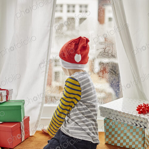 Christmas morning in a family home. A boy in a Santa hat looking out of a bedroom window. Christmas morning in a family home. A boy in a Santa hat looking out of a bedroom window.
