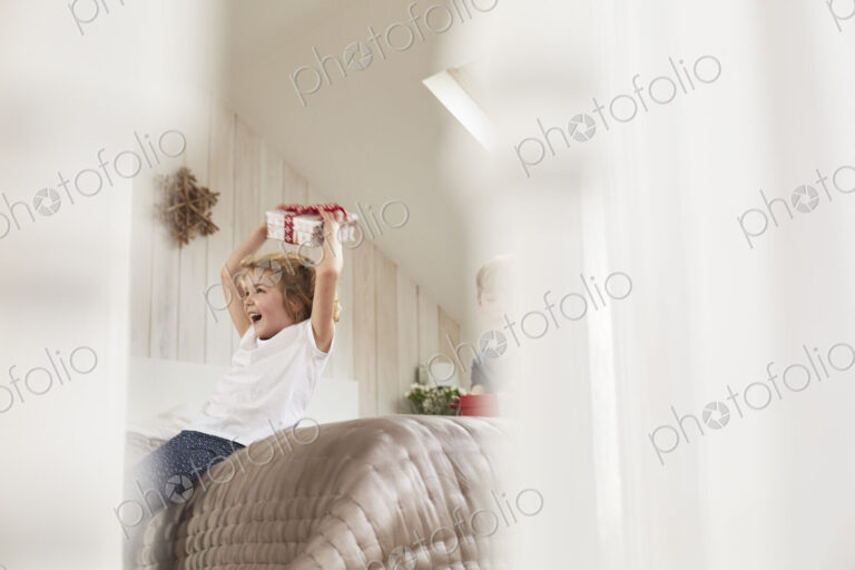 Christmas morning in a family home. A girl holding a present above her head.