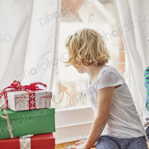 Christmas morning in a family home. A girl on a window seat looking out. Christmas morning in a family home. A girl on a window seat looking out.