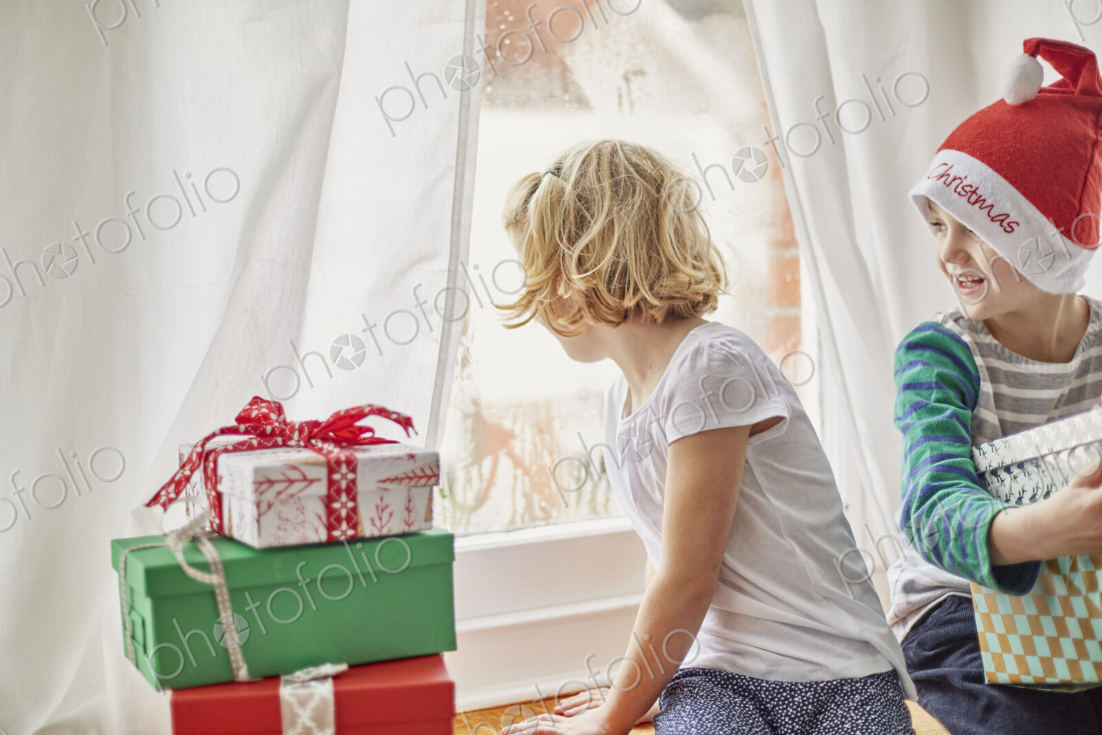 Christmas morning in a family home. A girl on a window seat looking out.