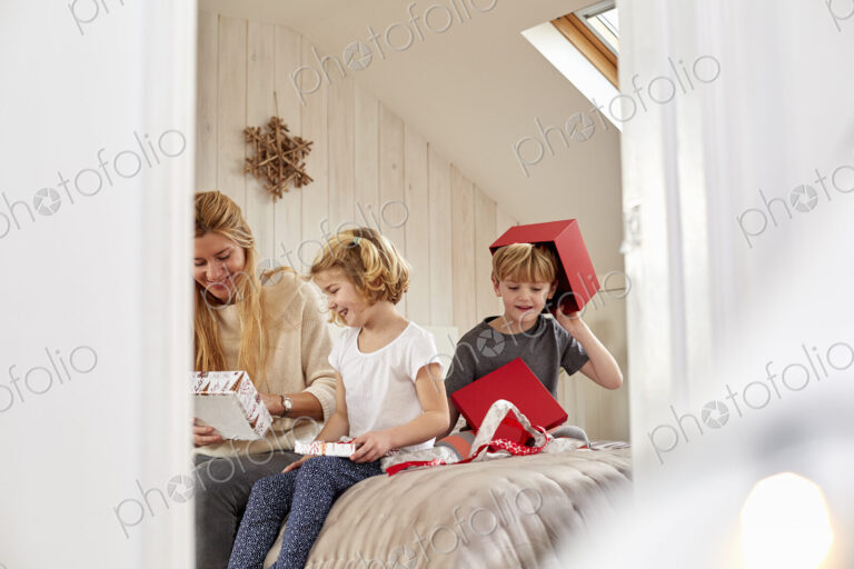 Christmas morning in a family home. A mother and two children sitting on a bed opening…