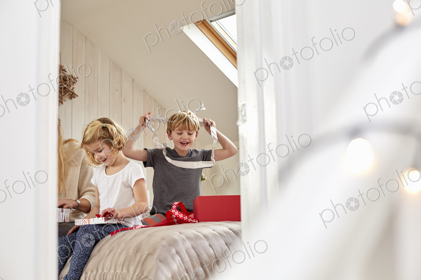 Christmas morning in a family home. A mother and two children sitting on a bed opening…