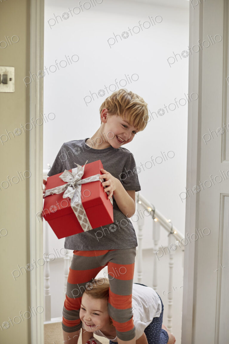 Christmas morning in a family home. Two children on the stairs carrying presents.