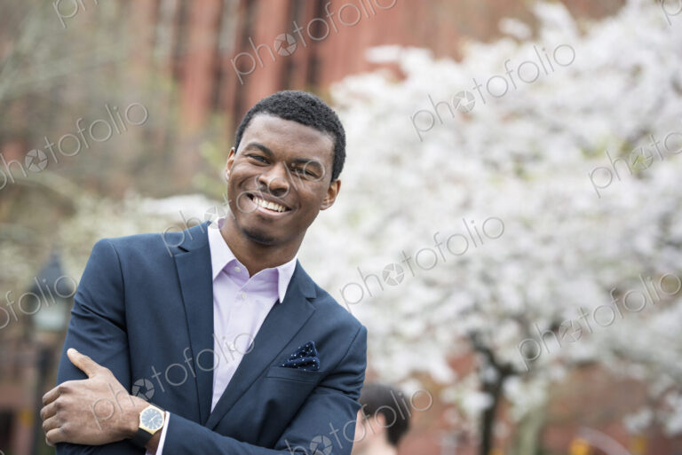 City life in spring. A man in a blue suit with arms folded, in a city park.