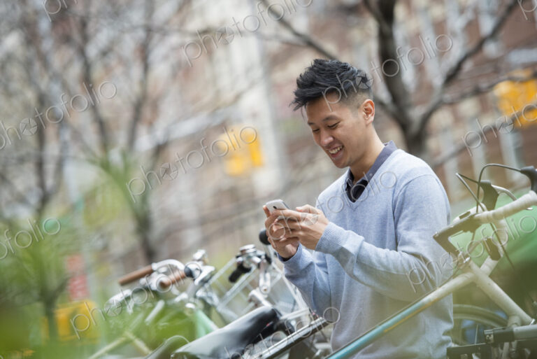 City life in spring. A man in a blue sweater by a row of parked bicycles. Checking his…