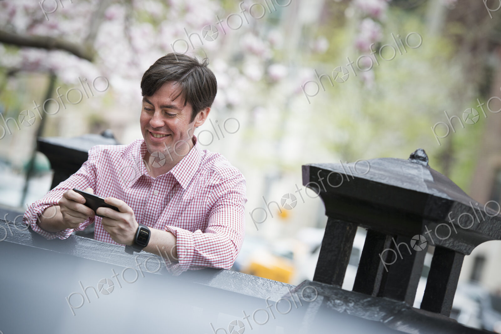 City life in spring. A man sitting outdoors in a city park. Looking down at his smart…