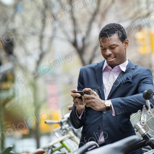 City life in spring. A young man in a blue suit, by a bicycle park. Checking his smart… City life in spring. A young man in a blue suit, by a bicycle park. Checking his smart…