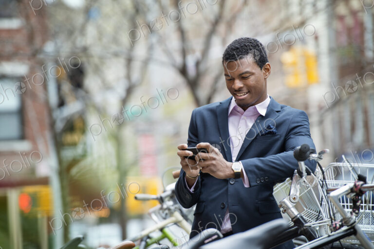City life in spring. A young man in a blue suit, by a bicycle park. Checking his smart…
