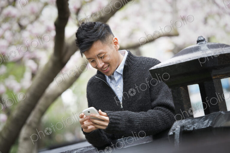 City life in spring. A young man outdoors in a city park. Sitting on a bench.