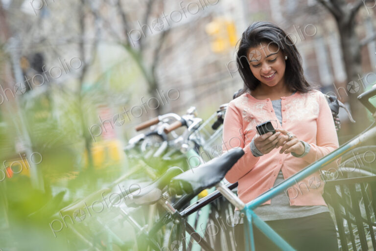 City life in spring. A young woman in a peach coloured shirt, using her smart phone.…