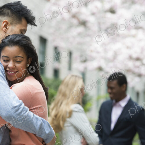 City life in spring. Young people outdoors in a city park. A couple embracing, and two… City life in spring. Young people outdoors in a city park. A couple embracing, and two…