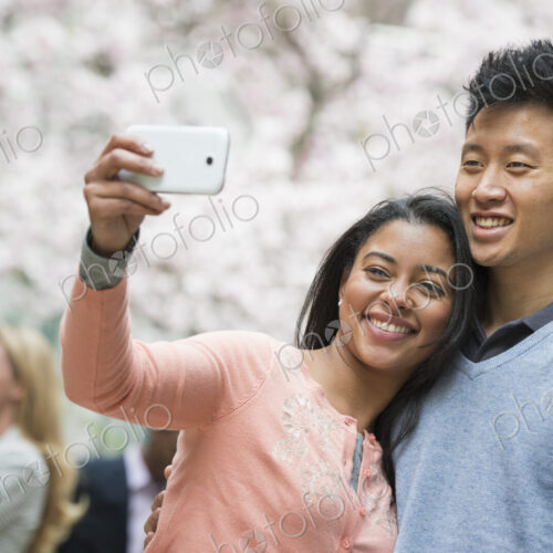 City life in spring. Young people outdoors in a city park. A couple taking a self… City life in spring. Young people outdoors in a city park. A couple taking a self…